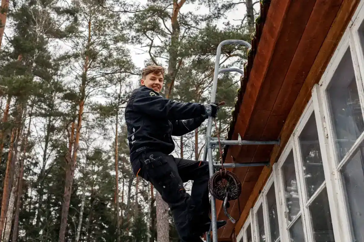 Nuohooja kiipeää tikkaille puutalon seinustalla talvella